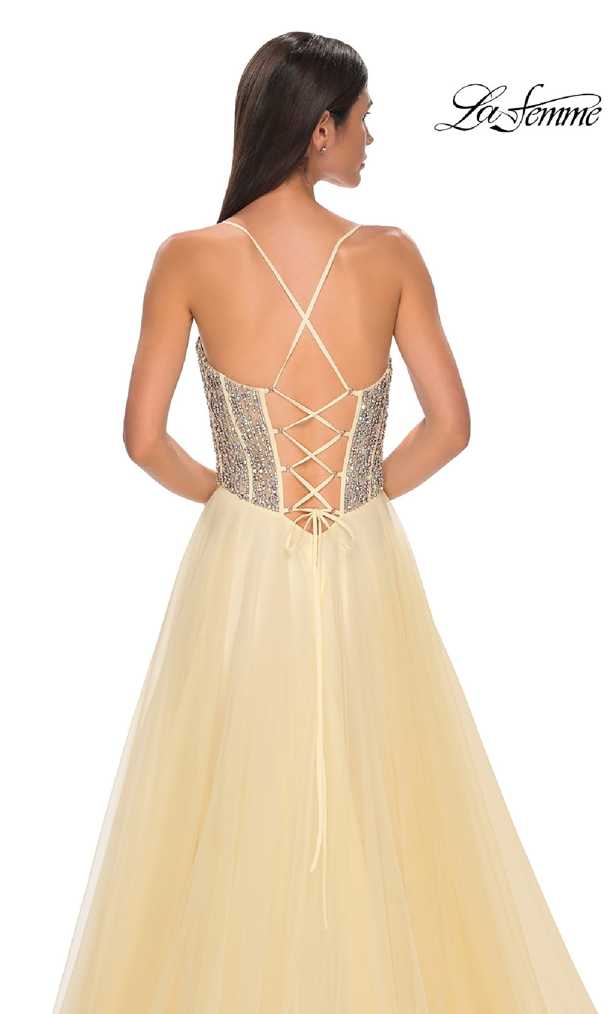 A woman in the La Femme 32703 Beaded-Corset Long Prom Dress, pale yellow with a rhinestone-beaded corset bodice, crisscross lace-up back, and flowing tulle skirt.